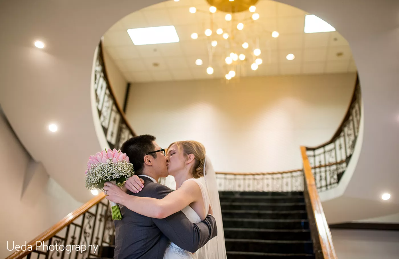 Kiss in front of the grand staircase by Ueda Photography