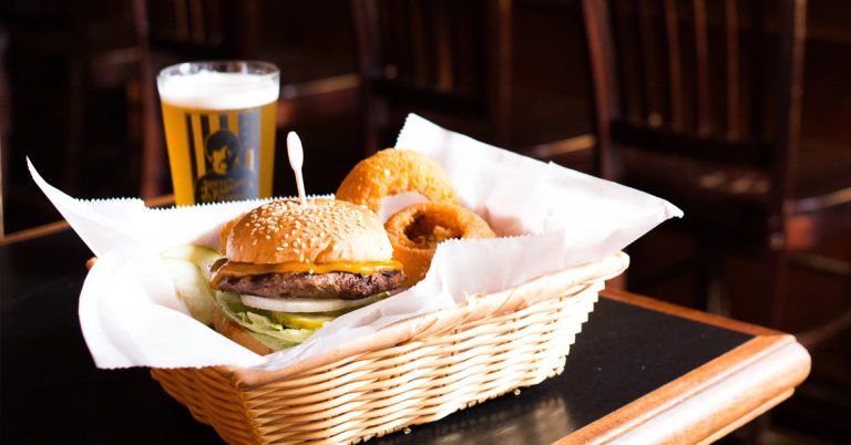 A cheeseburger and onion ring basket next to a pint of Beer showcasing what the menu has to offer at Dotty Dumpling's Dowry.